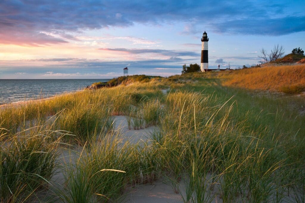 A lighthouse on the beach with grass in front of it.