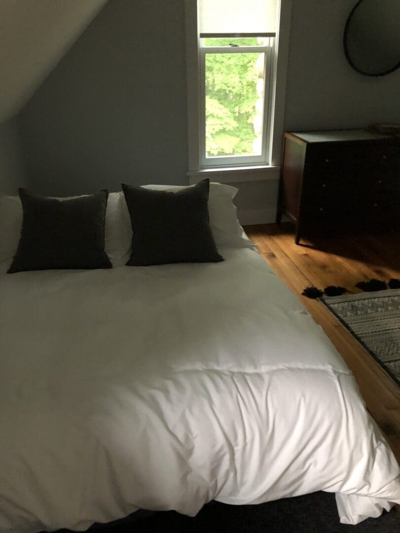 A bed with white sheets and pillows in front of a window.