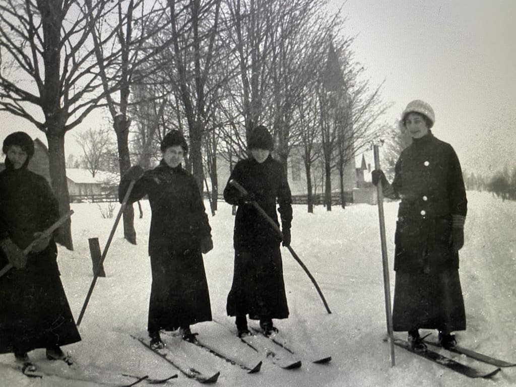 Three women in black coats and hats on skis.